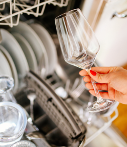 hand holding a wine glass outside of a clean dishwasher