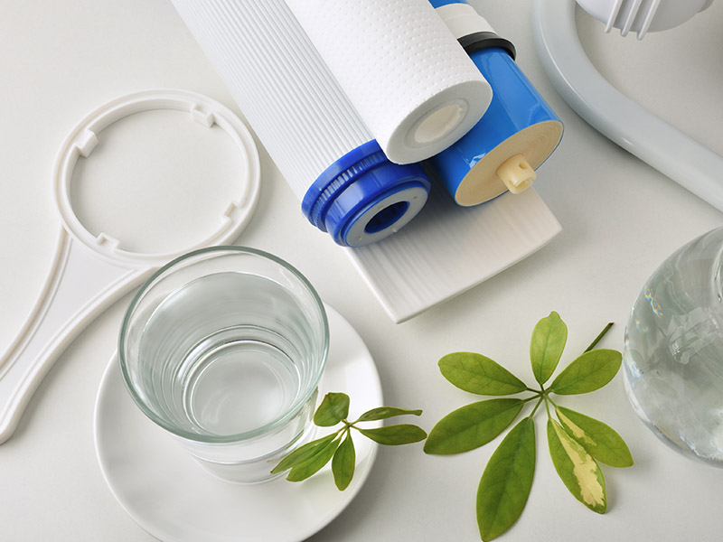 Clear glass of water, water filters, & filtration system equipment sitting on counter.
