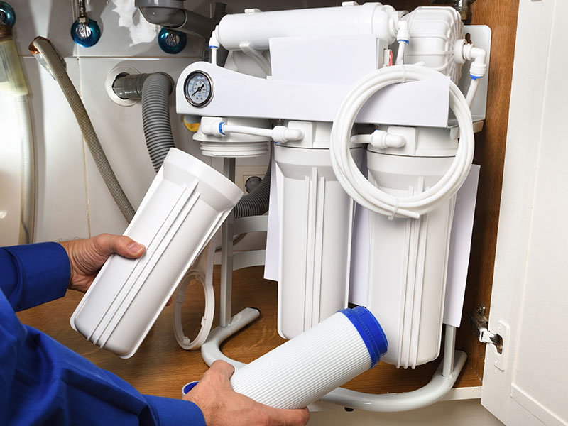 Technician replacing filters in a reverse osmosis filtration system.