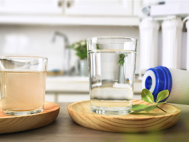 Water filtration comparison with cup of dirty water to one side and cup of clean water next to a filter on the other side.